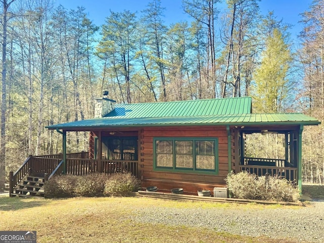 view of front of property featuring metal roof, a chimney, and log siding