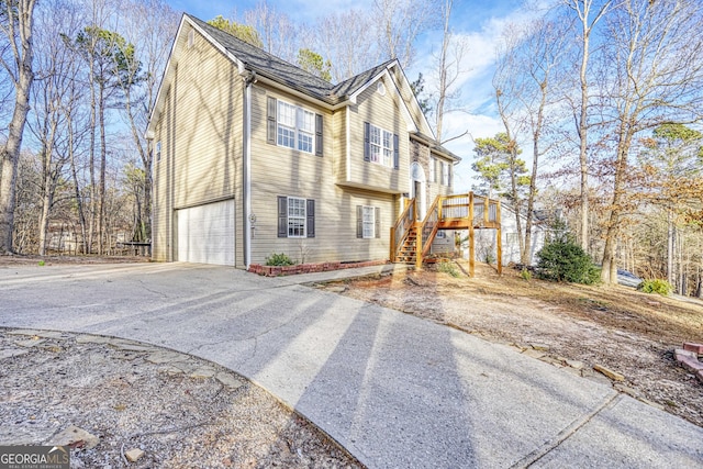 view of side of property with driveway, an attached garage, and stairway