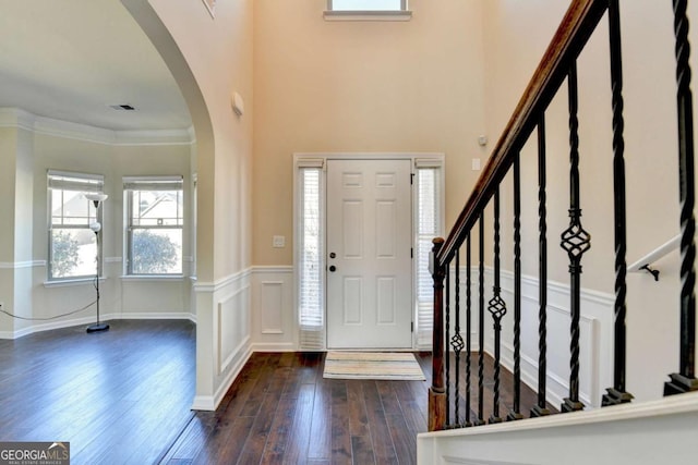 entrance foyer with arched walkways, a wainscoted wall, crown molding, dark wood finished floors, and visible vents