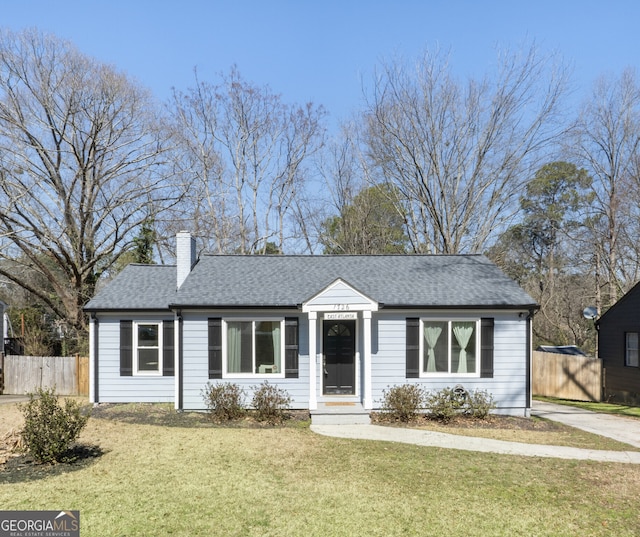 ranch-style house featuring a shingled roof, fence, a chimney, and a front lawn