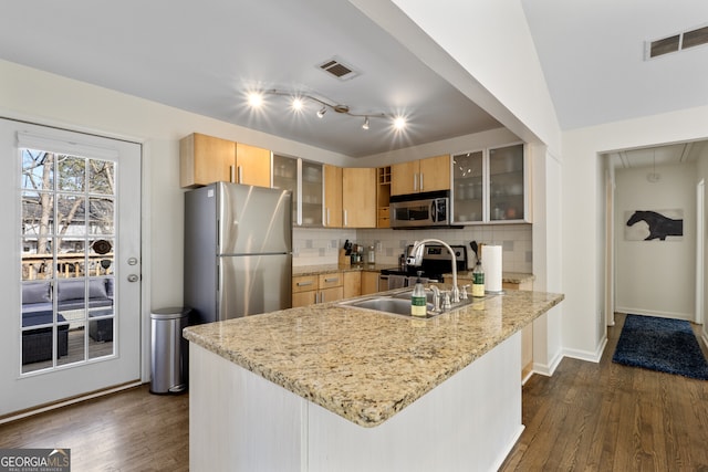 kitchen with light stone counters, stainless steel appliances, a peninsula, visible vents, and glass insert cabinets