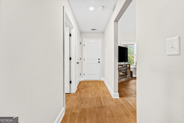 corridor with light wood finished floors, visible vents, and baseboards