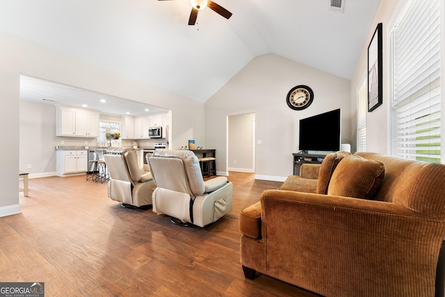 living area with high vaulted ceiling, light wood-type flooring, a ceiling fan, and baseboards