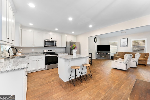 kitchen with a breakfast bar area, appliances with stainless steel finishes, white cabinetry, a sink, and a kitchen island