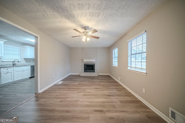 unfurnished living room with a sink, a fireplace, a textured ceiling, a ceiling fan, and visible vents