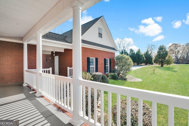 exterior space featuring roof with shingles, a porch, a lawn, and brick siding