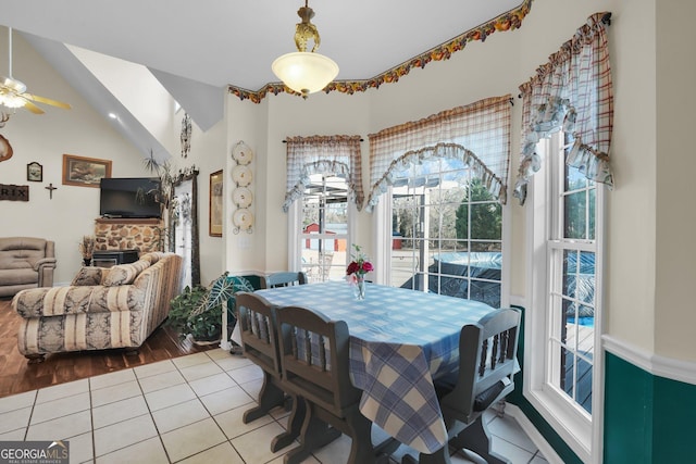 dining area with ceiling fan, a fireplace, vaulted ceiling, and light tile patterned flooring