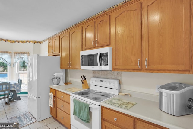 kitchen featuring light countertops, white appliances, brown cabinetry, and light tile patterned flooring