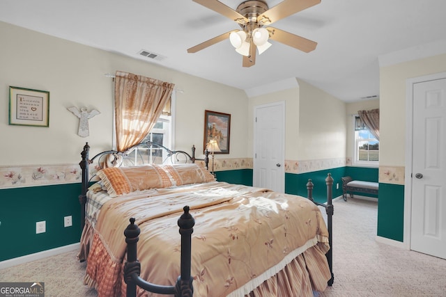 bedroom with light carpet, a wainscoted wall, ceiling fan, and visible vents