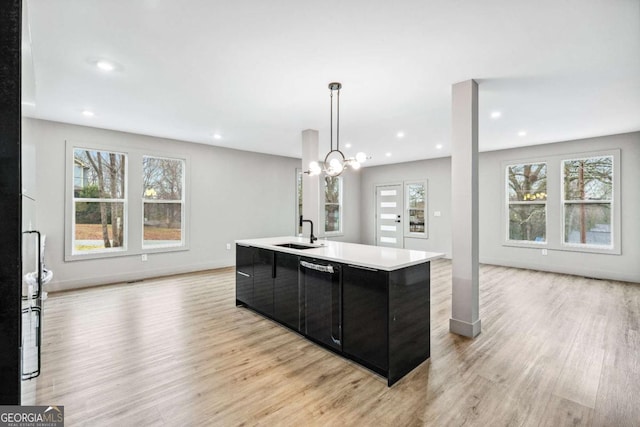 kitchen featuring decorative light fixtures, a center island with sink, light countertops, a sink, and modern cabinets