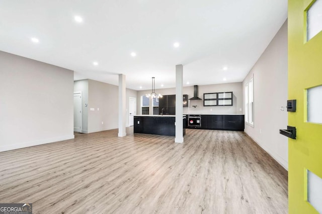 kitchen featuring wall chimney range hood, recessed lighting, light wood-style flooring, and a notable chandelier