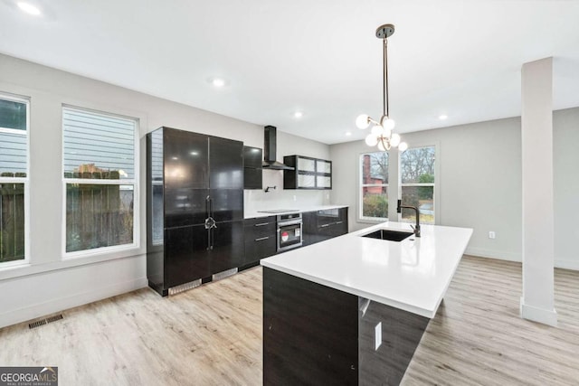 kitchen with decorative light fixtures, a sink, light countertops, black appliances, and a center island with sink