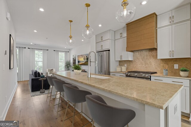 kitchen with premium appliances, light countertops, an island with sink, light wood-style flooring, and a chandelier