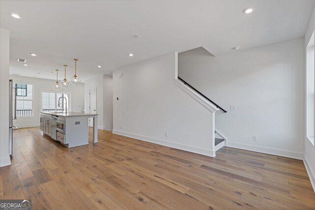 unfurnished living room with light wood-style flooring, baseboards, recessed lighting, stairway, and a sink
