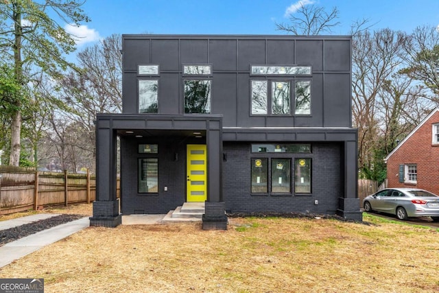 contemporary home featuring board and batten siding, a front yard, brick siding, and fence