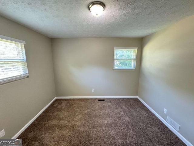 unfurnished room with a textured ceiling, carpet, visible vents, and baseboards