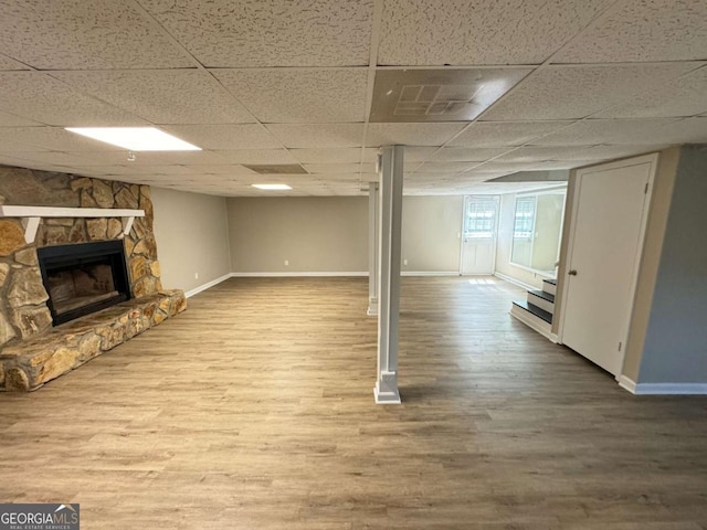 basement with a drop ceiling, a fireplace, baseboards, and wood finished floors