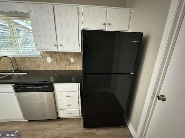 kitchen with dark countertops, freestanding refrigerator, white cabinets, a sink, and dishwashing machine