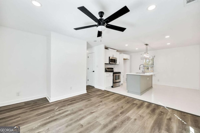 unfurnished living room featuring baseboards, recessed lighting, ceiling fan, a sink, and light wood-style floors