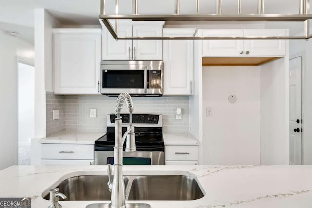 kitchen with light stone counters, a sink, white cabinetry, stainless steel appliances, and decorative backsplash