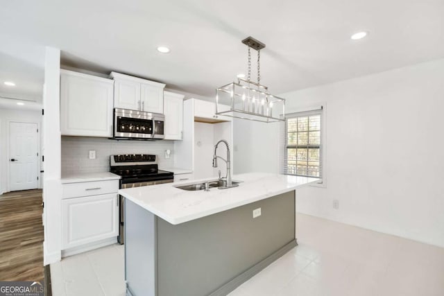 kitchen featuring an island with sink, a sink, decorative backsplash, appliances with stainless steel finishes, and white cabinetry