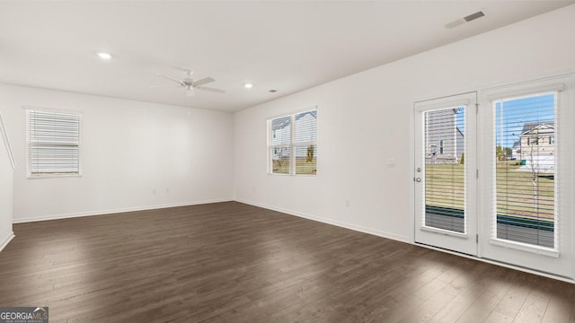 unfurnished room with a healthy amount of sunlight, baseboards, visible vents, and dark wood-style flooring