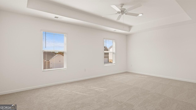 carpeted empty room featuring a ceiling fan, a tray ceiling, visible vents, and baseboards