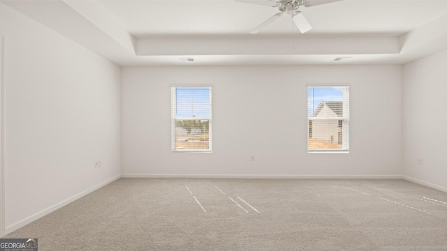 spare room featuring light carpet, baseboards, a tray ceiling, and a ceiling fan