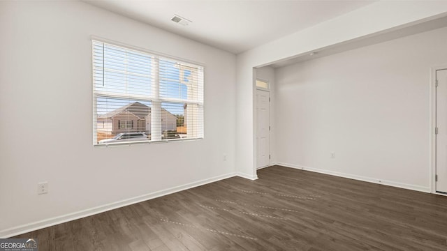 unfurnished room with dark wood-type flooring, visible vents, and baseboards