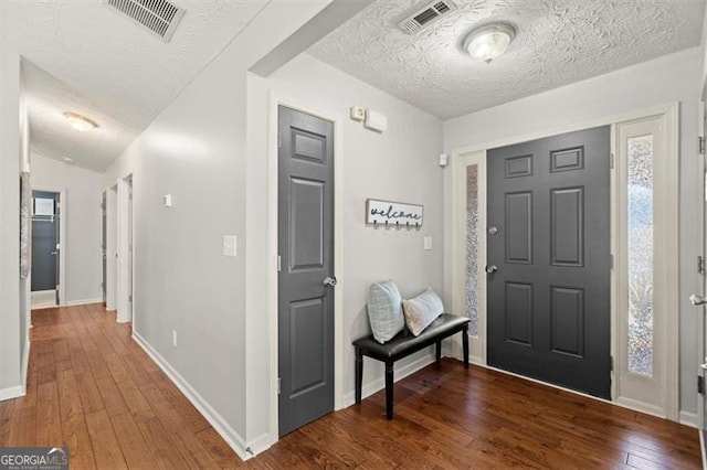 foyer with a textured ceiling, wood finished floors, visible vents, and baseboards