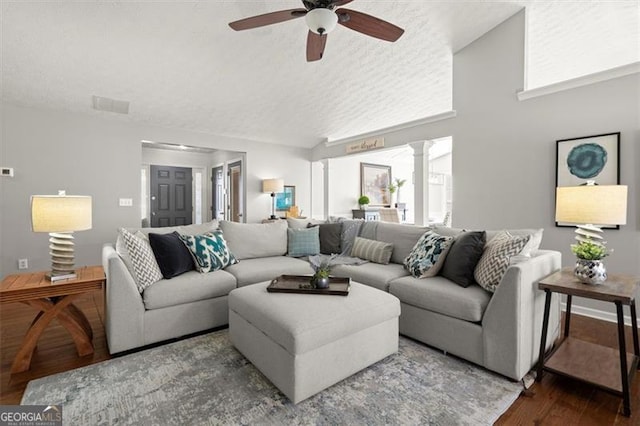 living room featuring a textured ceiling, dark wood-style flooring, visible vents, a ceiling fan, and decorative columns