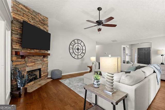 living room with lofted ceiling, ceiling fan, wood finished floors, a textured ceiling, and a fireplace