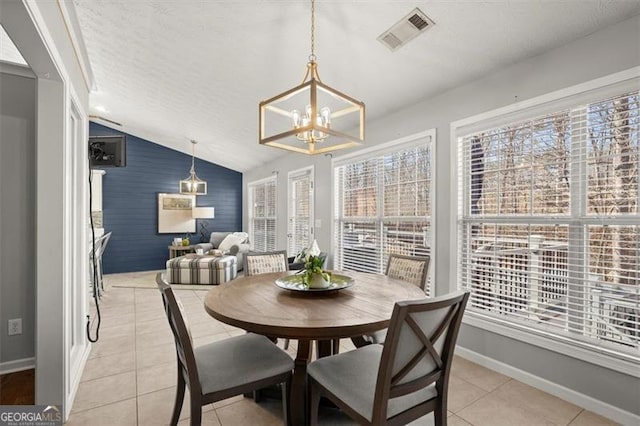 dining space featuring light tile patterned floors, visible vents, an accent wall, vaulted ceiling, and baseboards