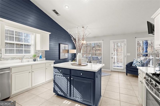 kitchen featuring light tile patterned floors, a kitchen island, white cabinets, light countertops, and appliances with stainless steel finishes