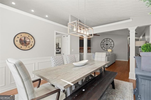 dining room featuring a wainscoted wall, wood finished floors, an inviting chandelier, crown molding, and a decorative wall