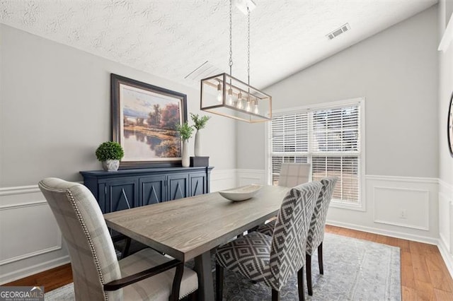 dining room featuring lofted ceiling, wainscoting, a textured ceiling, and light wood finished floors