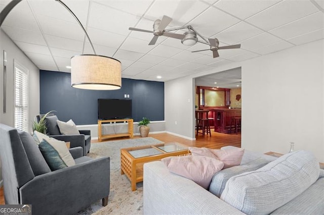 living room with ceiling fan, baseboards, a drop ceiling, and wood finished floors