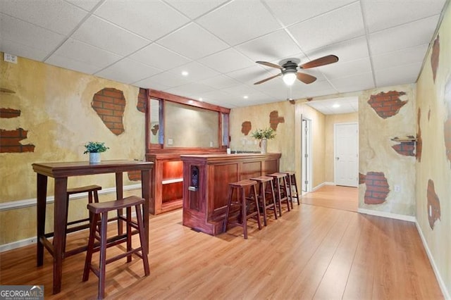 bar with light wood-style floors, a paneled ceiling, baseboards, and a dry bar