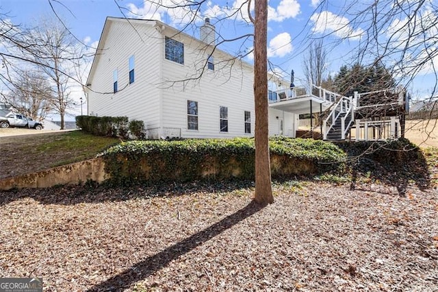 view of property exterior with a deck, a chimney, and stairs