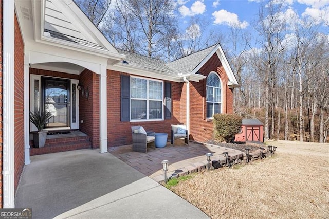 exterior space with brick siding, an outdoor structure, a storage shed, and roof with shingles