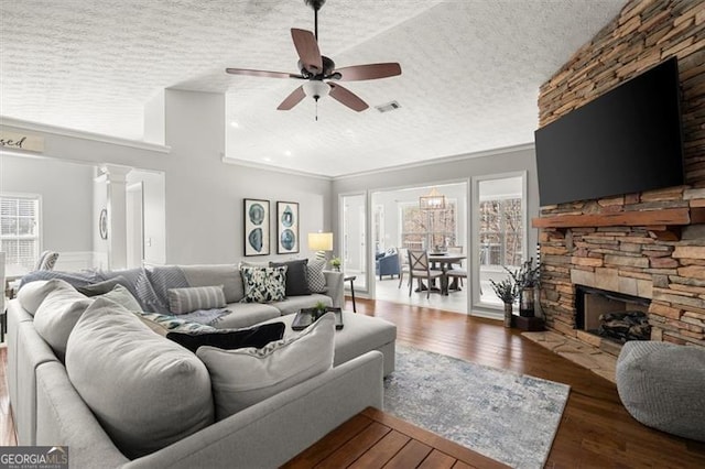 living area with a textured ceiling, a stone fireplace, dark wood-type flooring, and plenty of natural light