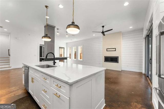 kitchen featuring light stone counters, open floor plan, a kitchen island with sink, white cabinets, and a sink