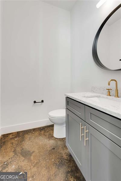 half bath featuring concrete flooring, toilet, vanity, and baseboards