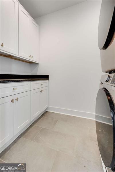 clothes washing area with stacked washing maching and dryer, cabinet space, and baseboards