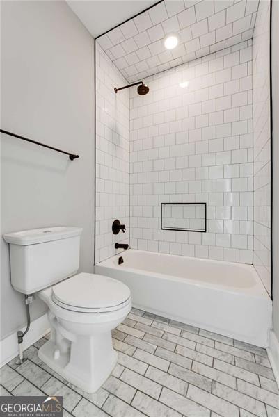 full bath with bathing tub / shower combination, toilet, and baseboards