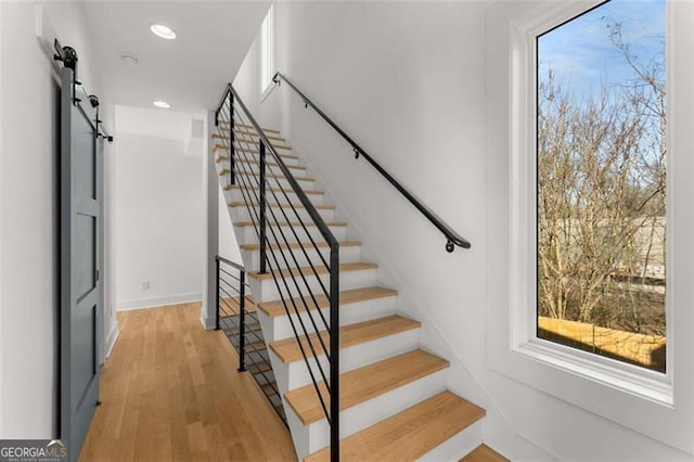 staircase featuring a barn door, wood finished floors, and recessed lighting