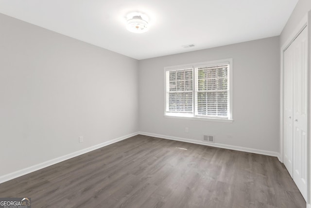 unfurnished bedroom with dark wood-type flooring, baseboards, visible vents, and a closet