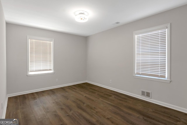 unfurnished room with dark wood-style floors, visible vents, and baseboards