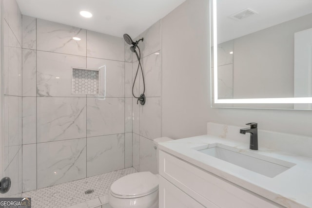 bathroom featuring visible vents, toilet, vanity, and tiled shower