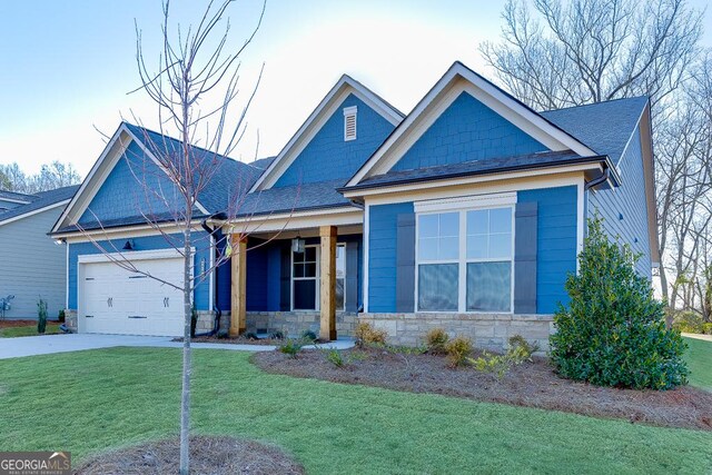 view of front of home featuring an attached garage, a shingled roof, stone siding, driveway, and a front yard